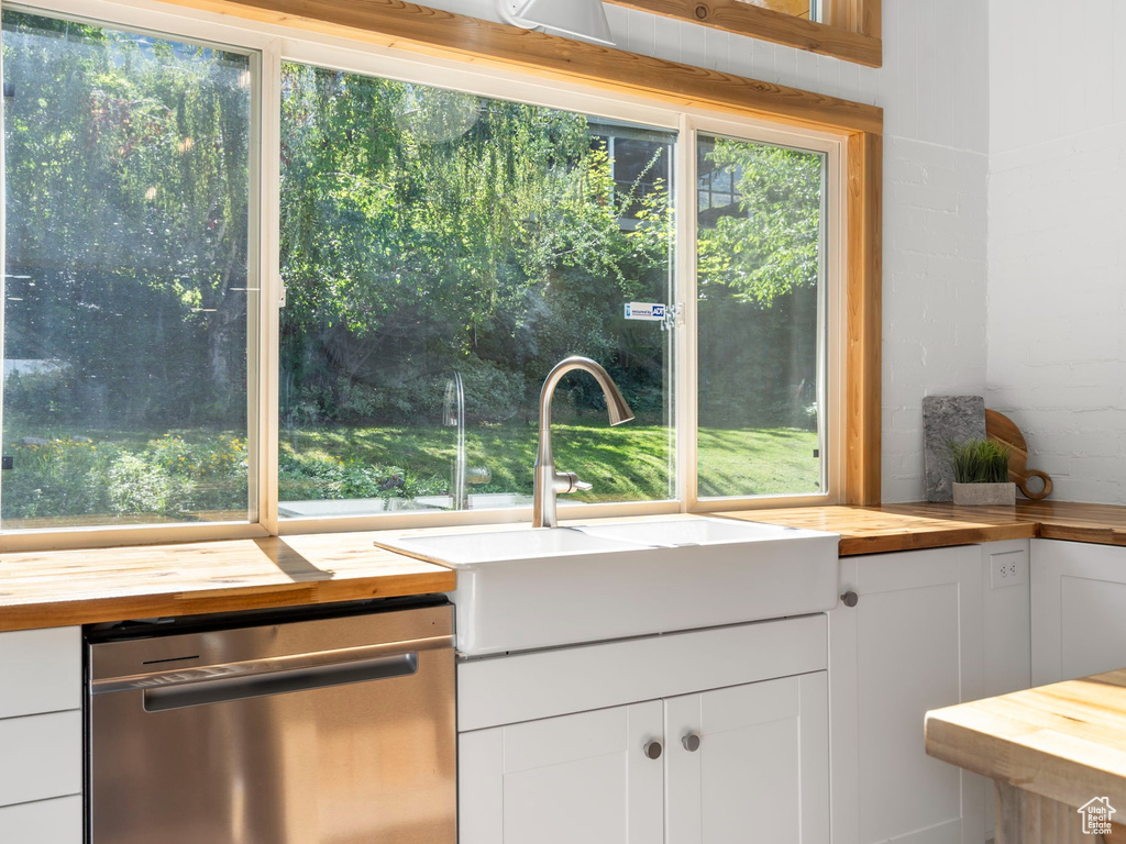 Kitchen with stainless steel dishwasher, white cabinetry, and butcher block countertops