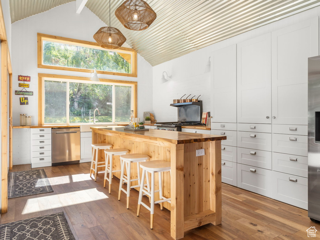 Kitchen with white cabinetry, stainless steel appliances, wooden counters, wood-type flooring, and a breakfast bar