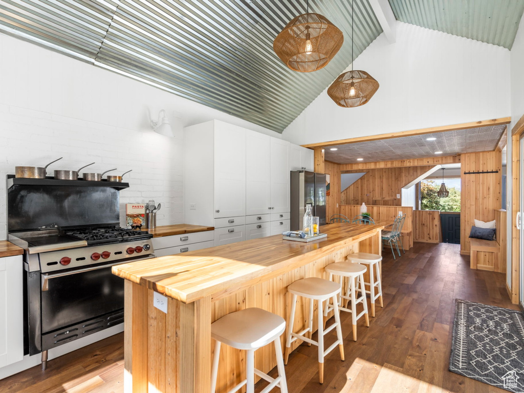 Kitchen with white cabinetry, lofted ceiling, stainless steel appliances, butcher block countertops, and wooden walls