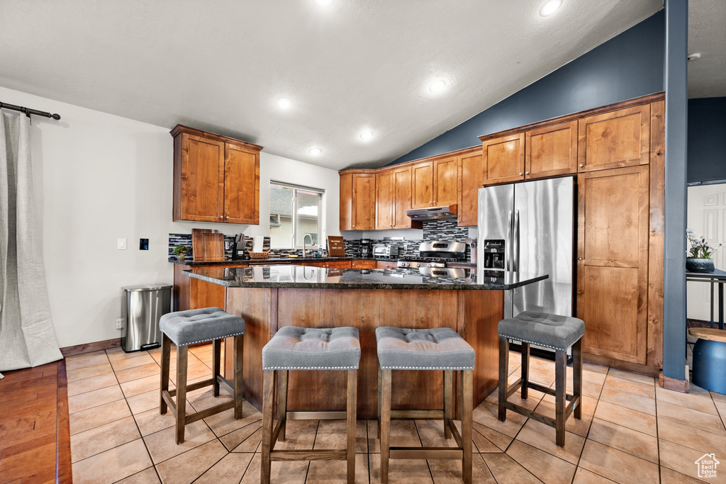 Kitchen featuring a center island, light tile flooring, dark stone countertops, and stainless steel fridge