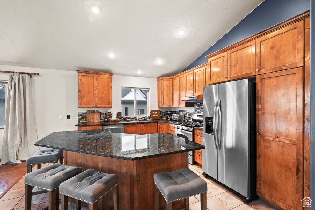 Kitchen featuring dark stone countertops, a kitchen island, appliances with stainless steel finishes, a kitchen bar, and light tile floors