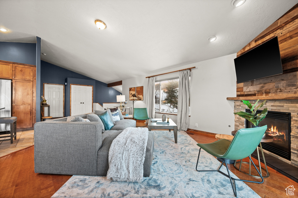 Living room with a stone fireplace, vaulted ceiling, and wood-type flooring