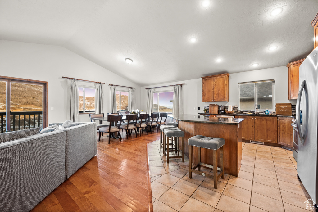 Kitchen with light hardwood / wood-style floors, a kitchen island, a breakfast bar area, stainless steel refrigerator, and vaulted ceiling