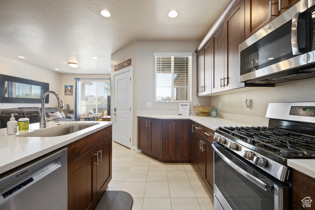 Kitchen featuring light stone countertops, dark brown cabinets, light tile floors, sink, and appliances with stainless steel finishes