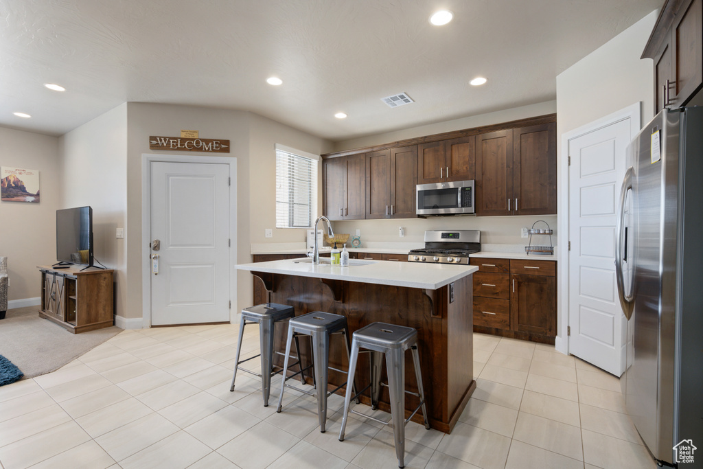 Kitchen featuring a center island with sink, light tile floors, sink, a kitchen bar, and appliances with stainless steel finishes