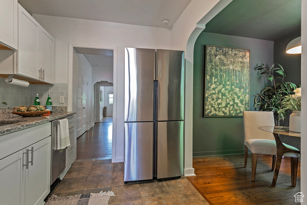 Kitchen with white cabinetry, stainless steel appliances, light stone counters, tasteful backsplash, and dark tile flooring