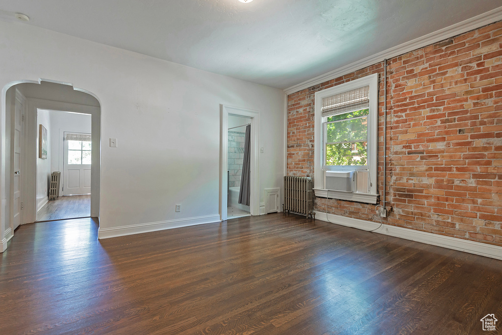 Spare room featuring brick wall, dark wood-type flooring, plenty of natural light, and radiator