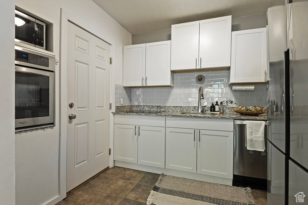 Kitchen featuring backsplash, dark tile flooring, sink, white cabinetry, and appliances with stainless steel finishes