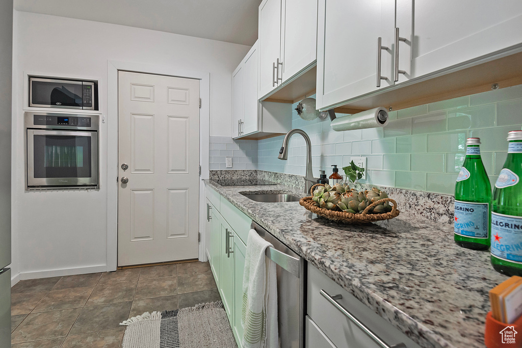 Kitchen featuring stainless steel appliances, tasteful backsplash, dark tile flooring, white cabinets, and sink