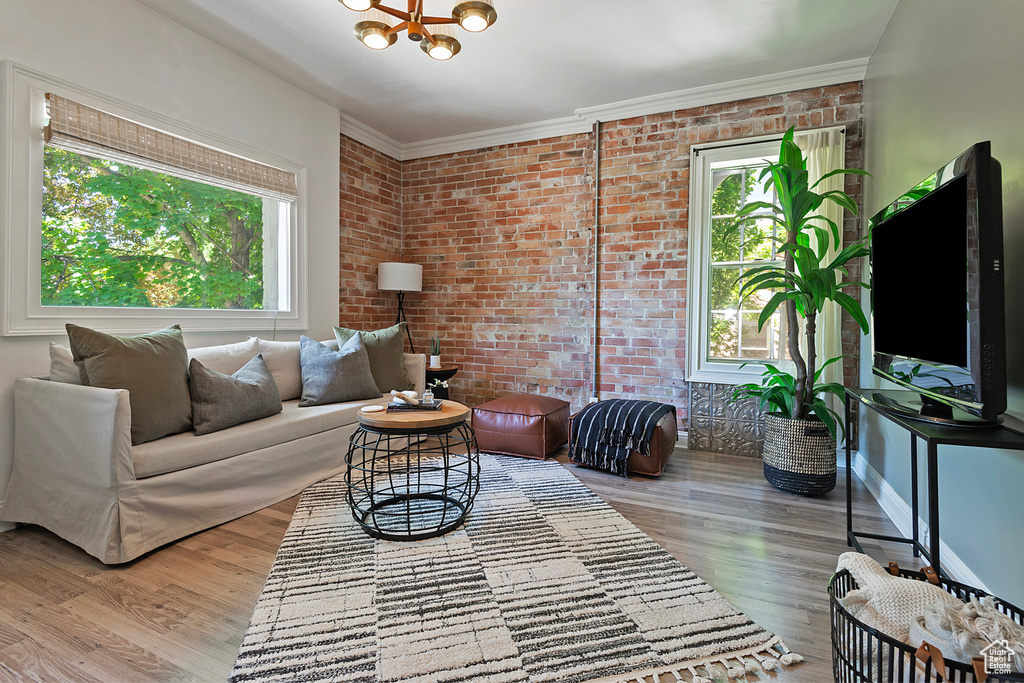 Living room with hardwood / wood-style flooring, brick wall, and an inviting chandelier