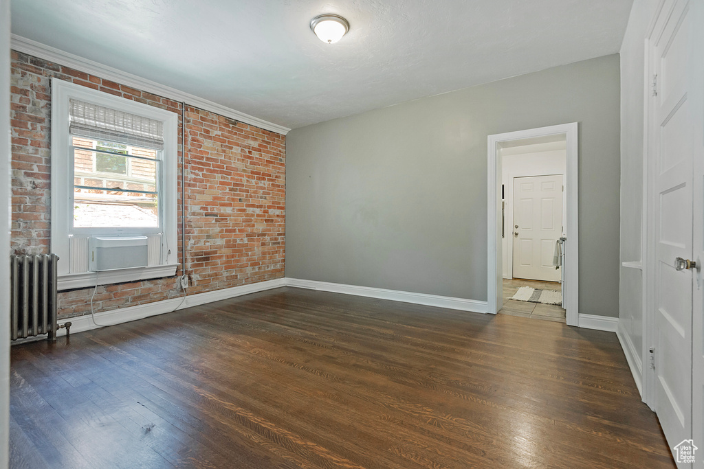 Spare room featuring dark hardwood / wood-style flooring, radiator heating unit, and brick wall