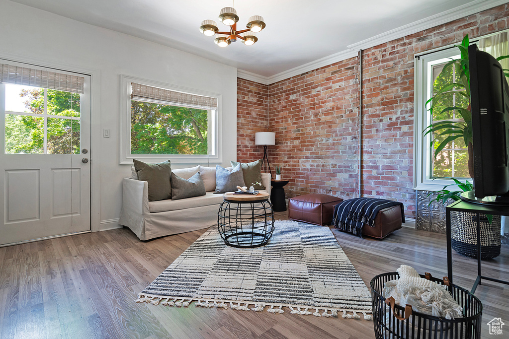 Living room featuring ornamental molding, light hardwood / wood-style flooring, an inviting chandelier, and brick wall