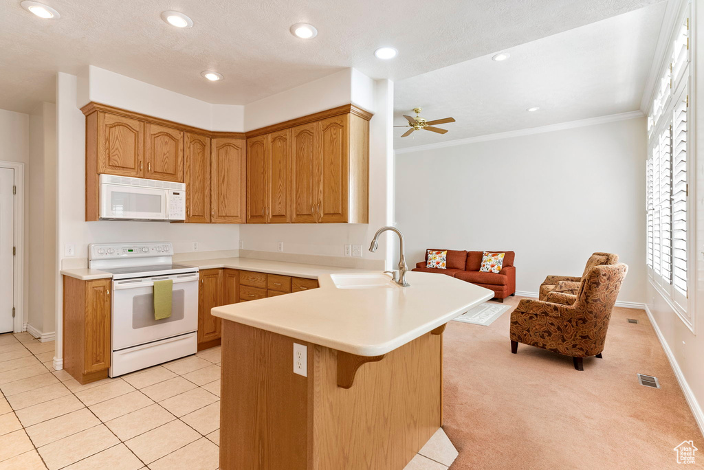 Kitchen with ceiling fan, kitchen peninsula, white appliances, light colored carpet, and sink