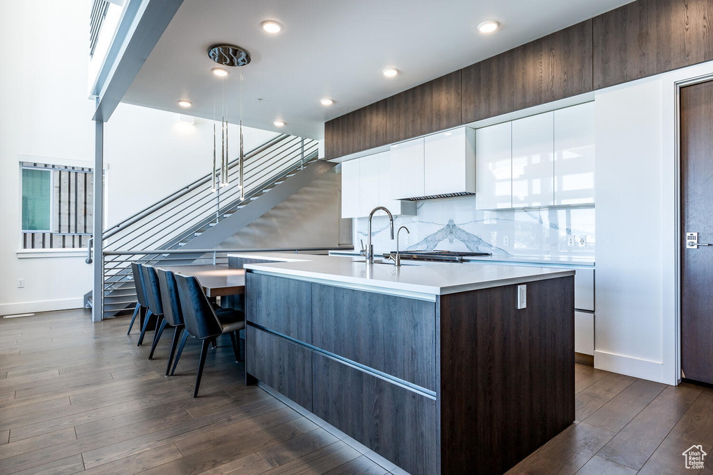 Kitchen with backsplash, dark wood-type flooring, white cabinetry, and an island with sink