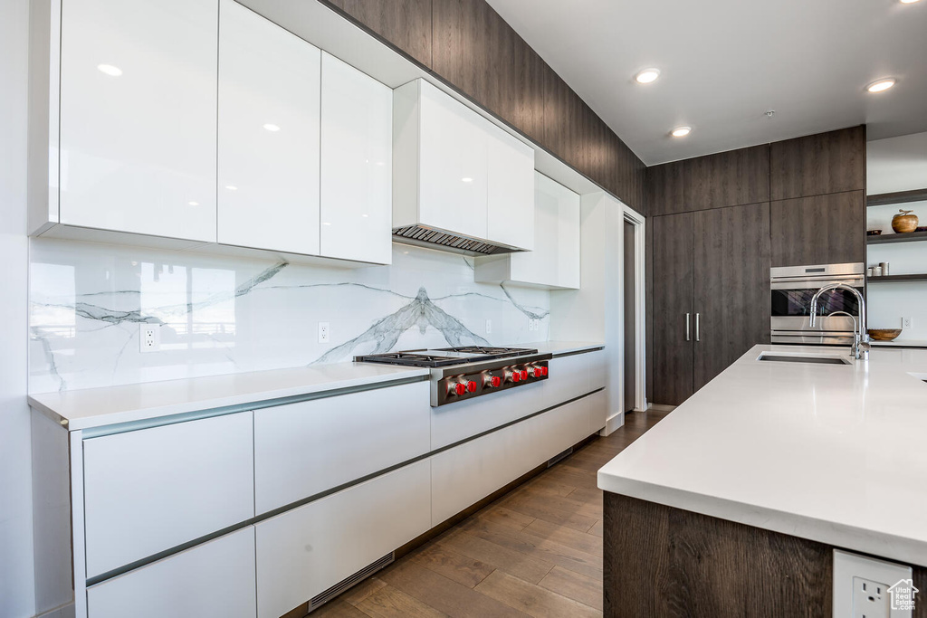 Kitchen with dark hardwood / wood-style floors, stainless steel appliances, backsplash, sink, and white cabinets