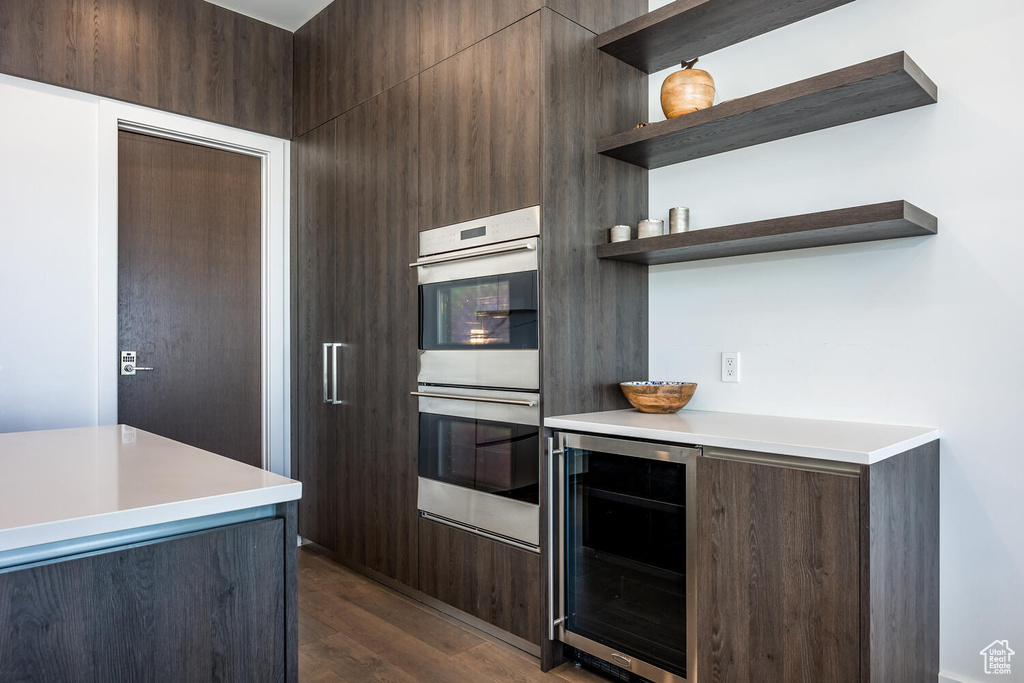 Kitchen featuring double oven, wine cooler, dark brown cabinetry, and dark wood-type flooring