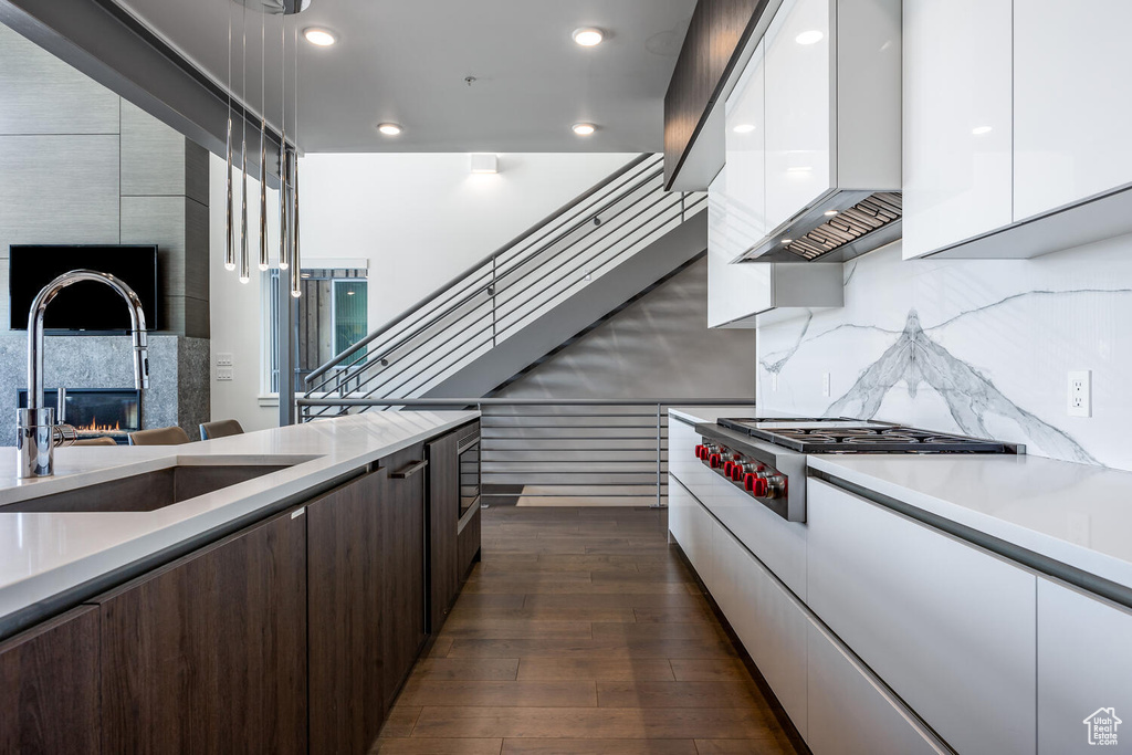 Kitchen with custom exhaust hood, luxury stove, dark hardwood / wood-style flooring, sink, and white cabinets