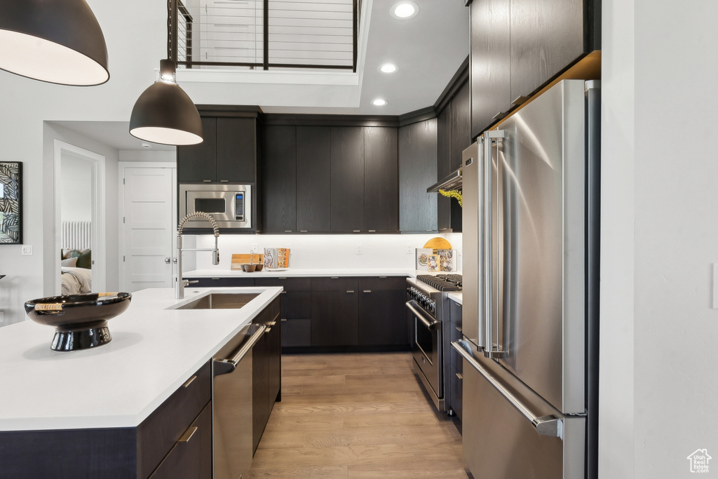 Kitchen featuring hanging light fixtures, high quality appliances, a center island with sink, light hardwood / wood-style flooring, and sink