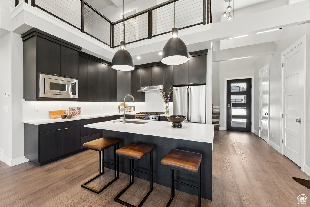 Kitchen with a center island with sink, light hardwood / wood-style flooring, appliances with stainless steel finishes, pendant lighting, and a towering ceiling