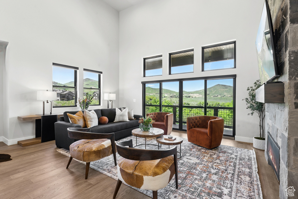 Living room with a high ceiling, a stone fireplace, plenty of natural light, and wood-type flooring