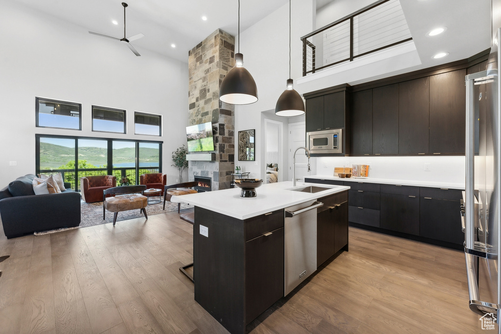 Kitchen with light hardwood / wood-style floors, a kitchen island with sink, pendant lighting, a stone fireplace, and a towering ceiling