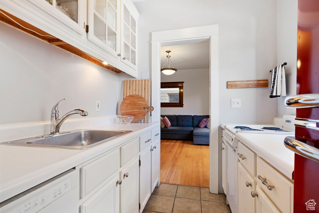 Kitchen featuring sink, white appliances, light tile patterned flooring, and white cabinetry