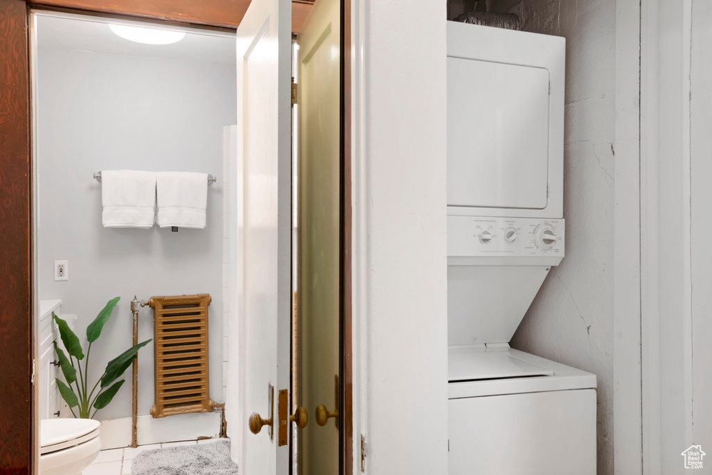 Clothes washing area featuring stacked washer / dryer, radiator heating unit, and light tile patterned floors