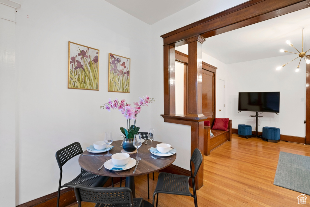 Dining room with a notable chandelier, light hardwood / wood-style floors, and ornate columns