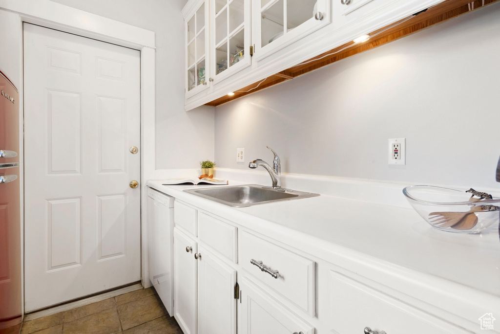 Kitchen featuring light tile patterned floors, sink, white dishwasher, and white cabinets