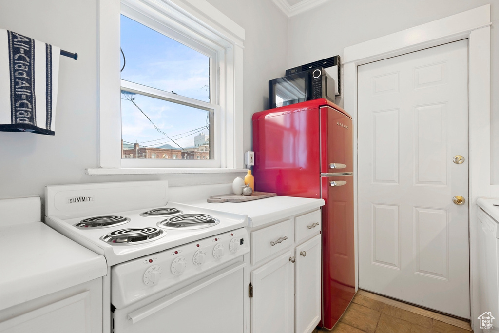 Kitchen featuring fridge, white range, white cabinetry, light tile patterned floors, and crown molding