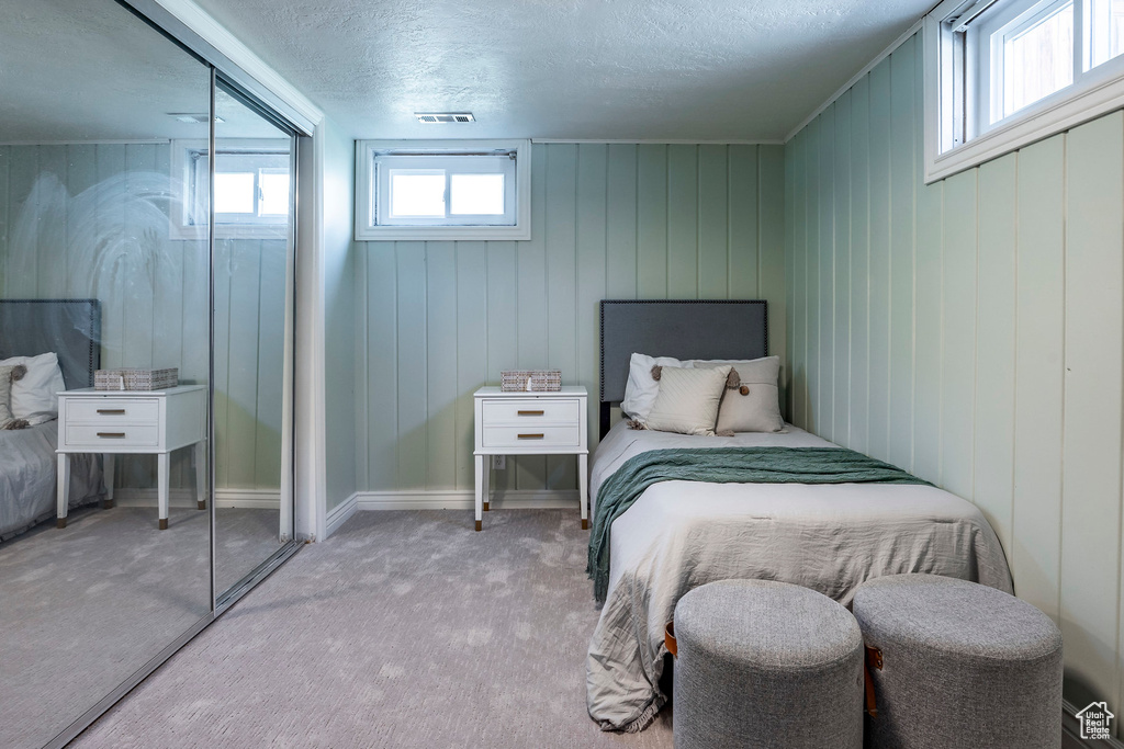 Bedroom with a closet, wooden walls, light carpet, and a textured ceiling