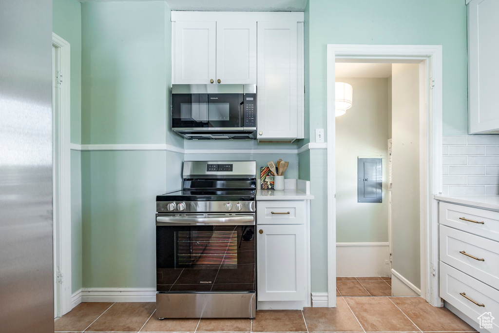 Kitchen featuring electric panel, stainless steel appliances, light tile patterned floors, and white cabinets