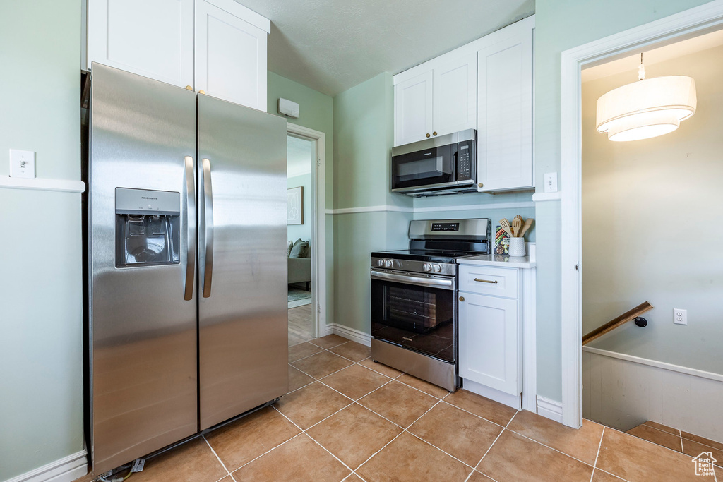 Kitchen with appliances with stainless steel finishes, light tile patterned floors, and white cabinets