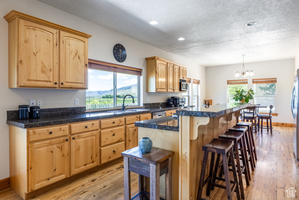 Kitchen with light hardwood / wood-style flooring, stainless steel appliances, decorative light fixtures, and a breakfast bar