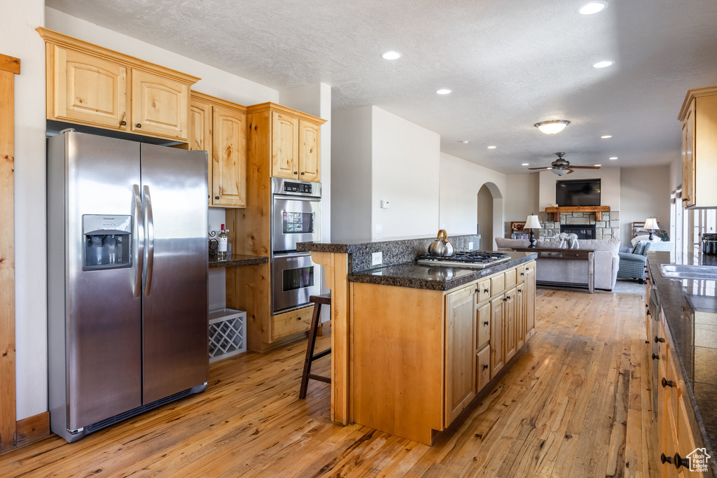 Kitchen with light hardwood / wood-style floors, appliances with stainless steel finishes, ceiling fan, and a kitchen breakfast bar