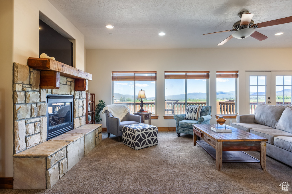 Living room with a stone fireplace, carpet, french doors, a textured ceiling, and ceiling fan