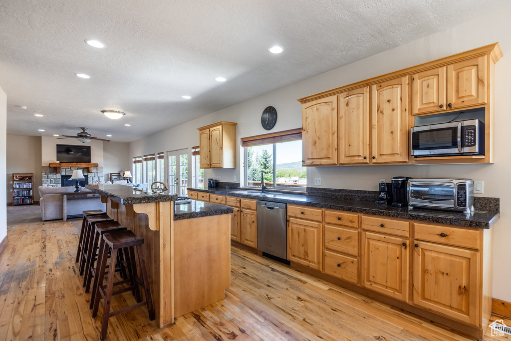 Kitchen with ceiling fan, light wood-type flooring, a center island, a breakfast bar, and appliances with stainless steel finishes