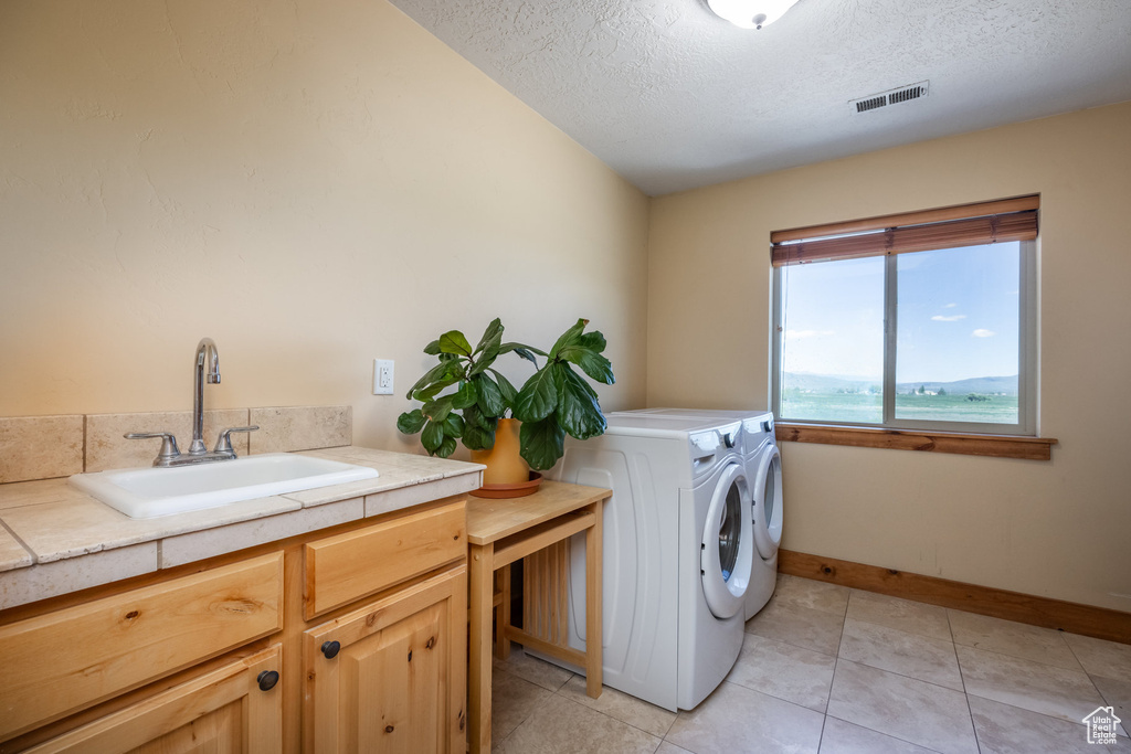 Washroom with sink, a textured ceiling, light tile patterned floors, and independent washer and dryer