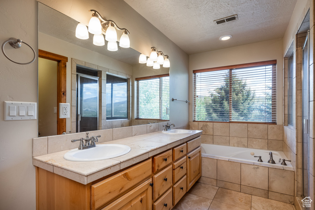 Bathroom with tiled bath, tile patterned floors, a textured ceiling, and double vanity