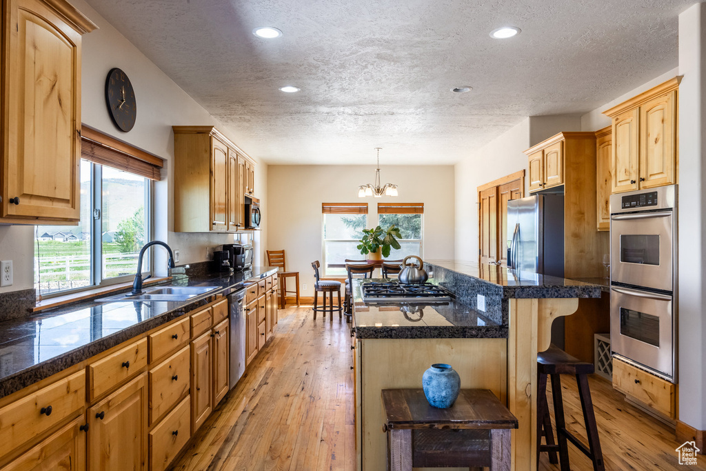 Kitchen with a kitchen bar, stainless steel appliances, light hardwood / wood-style floors, decorative light fixtures, and a kitchen island