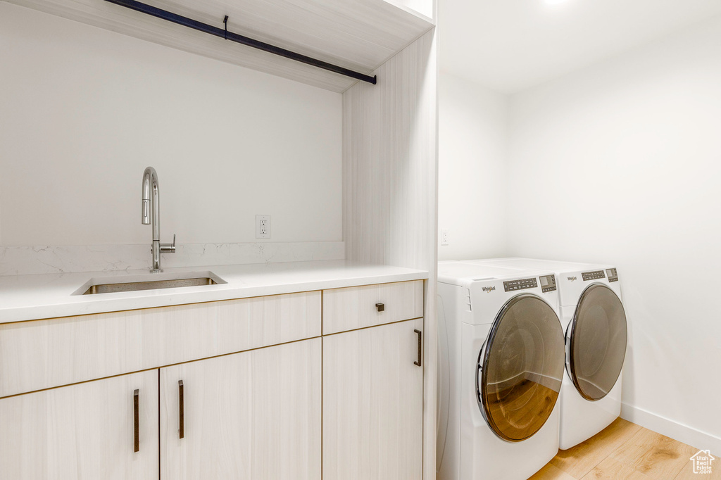 Laundry area featuring baseboards, light wood-style floors, independent washer and dryer, cabinet space, and a sink