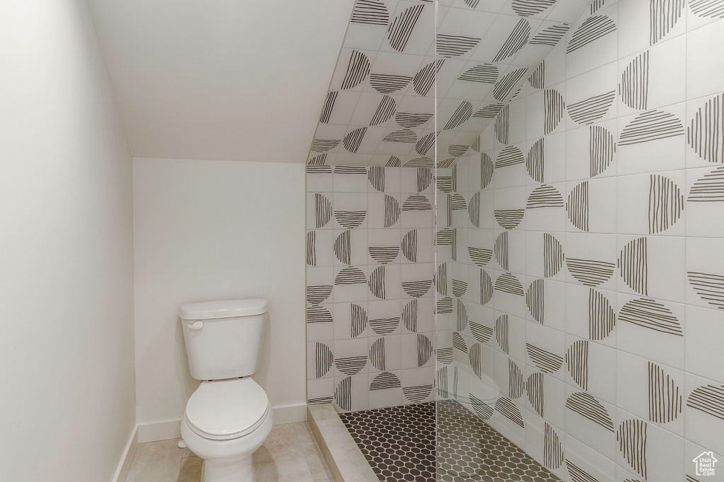 Bathroom with toilet, tile patterned floors, tiled shower, and baseboards