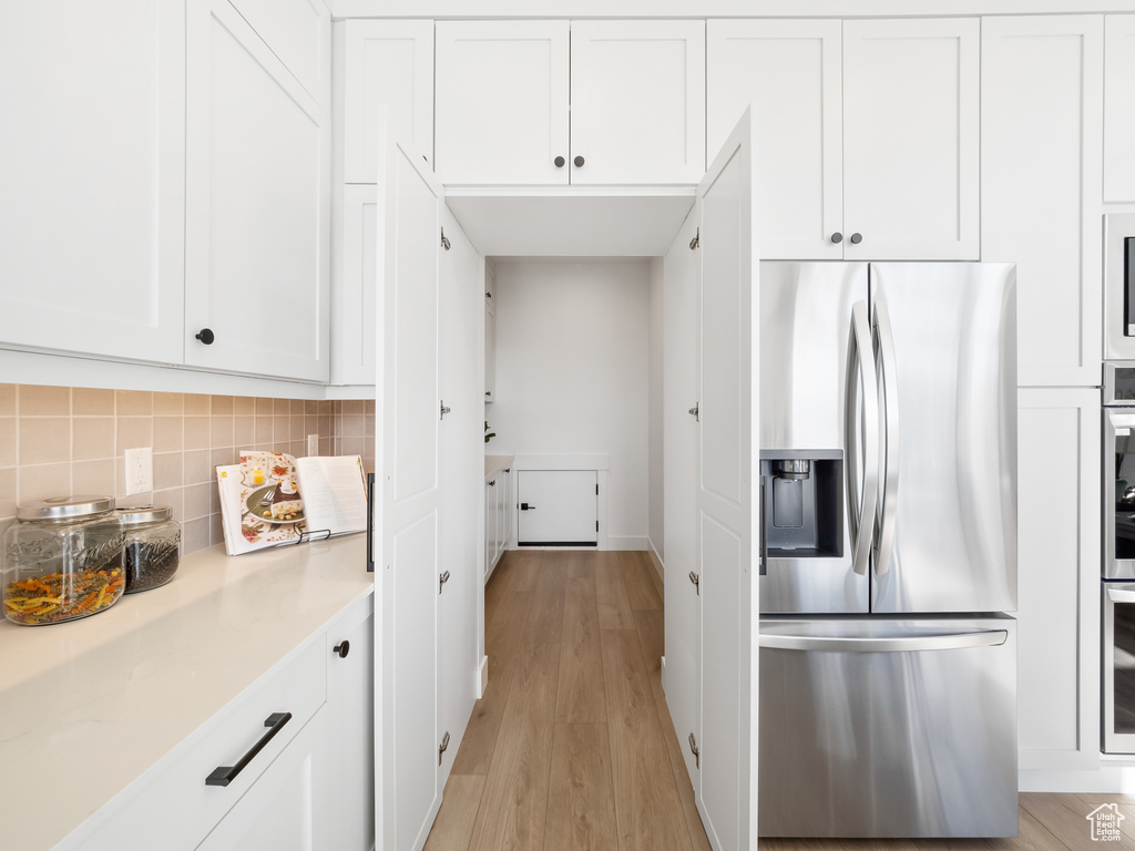 Kitchen with appliances with stainless steel finishes, light hardwood / wood-style flooring, white cabinetry, and tasteful backsplash