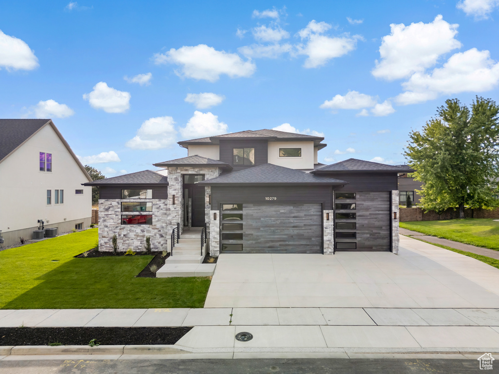 Prairie-style house featuring a front lawn, central AC, and a garage