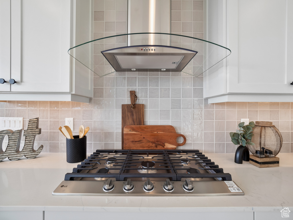 Kitchen with wall chimney exhaust hood, decorative backsplash, light stone countertops, and white cabinets