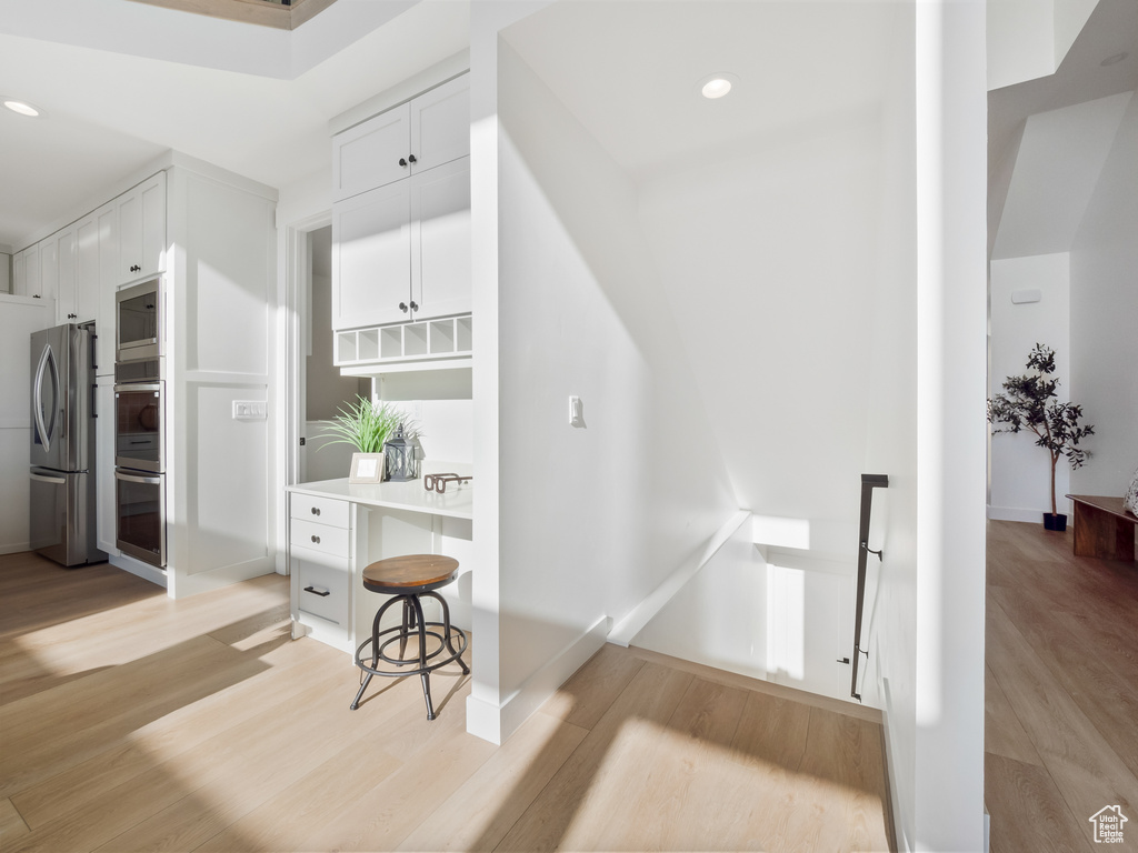 Interior space featuring light hardwood / wood-style floors, stainless steel appliances, a kitchen breakfast bar, and white cabinetry