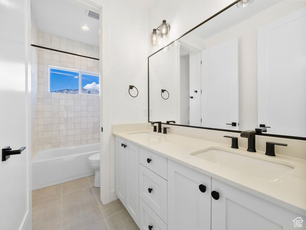 Full bathroom featuring toilet, double vanity, tiled shower / bath combo, and tile patterned floors