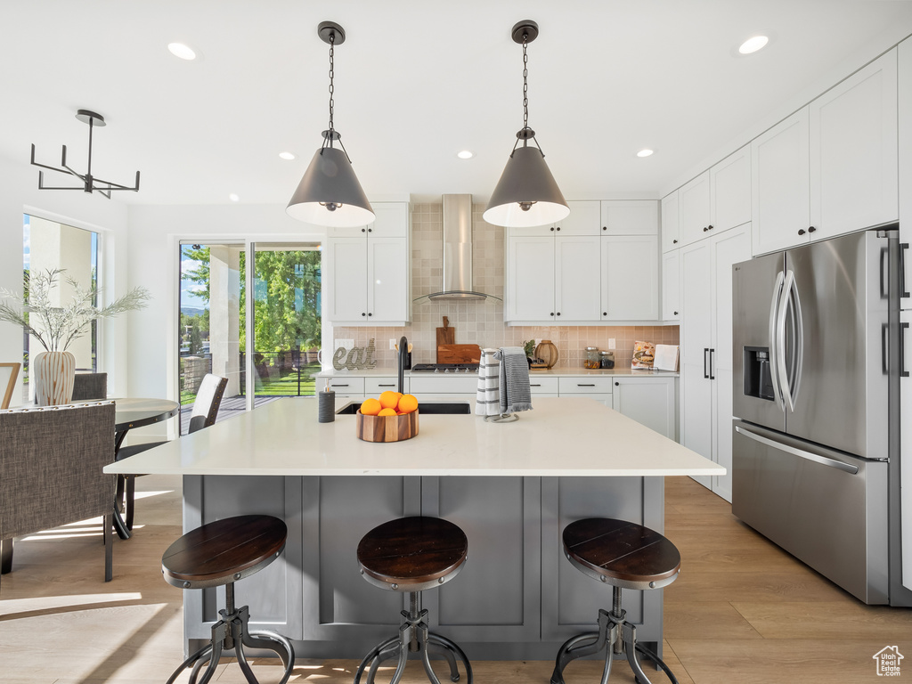 Kitchen with stainless steel refrigerator with ice dispenser, tasteful backsplash, wall chimney exhaust hood, and decorative light fixtures