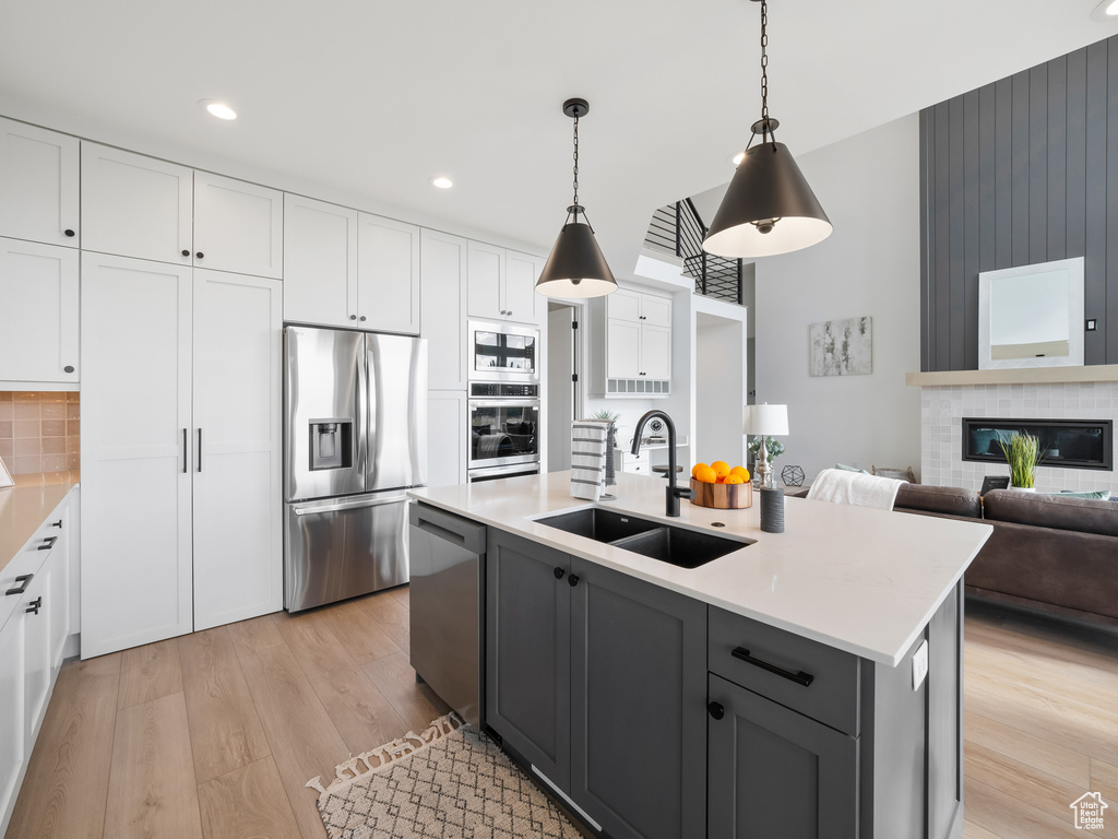 Kitchen featuring light hardwood / wood-style flooring, hanging light fixtures, white cabinets, appliances with stainless steel finishes, and sink