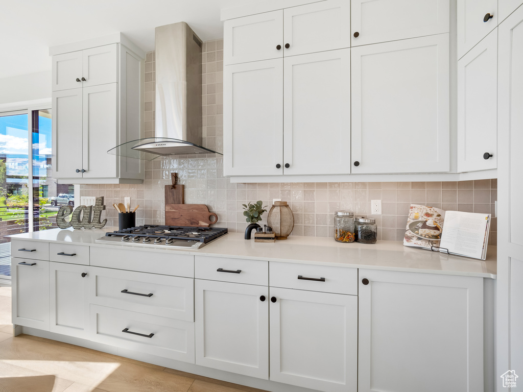 Kitchen featuring wall chimney exhaust hood, decorative backsplash, stainless steel gas cooktop, and white cabinets